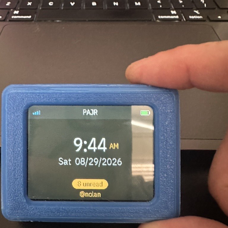 A PAJR device held in one hand, showing the time and eight unread messages
